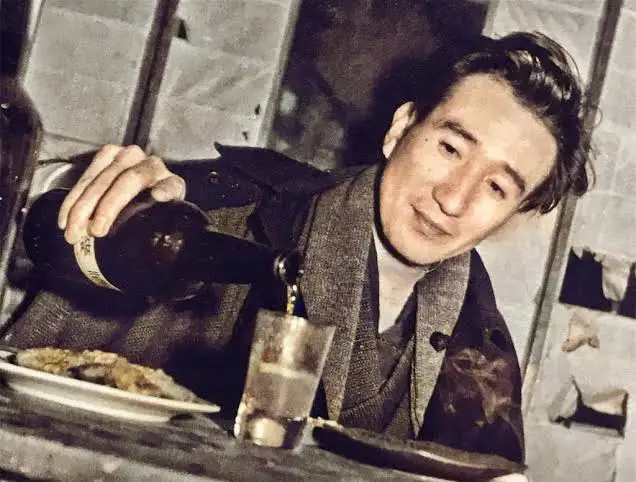 Osamu Dazai przy stole, nalewający napój do szklanki
